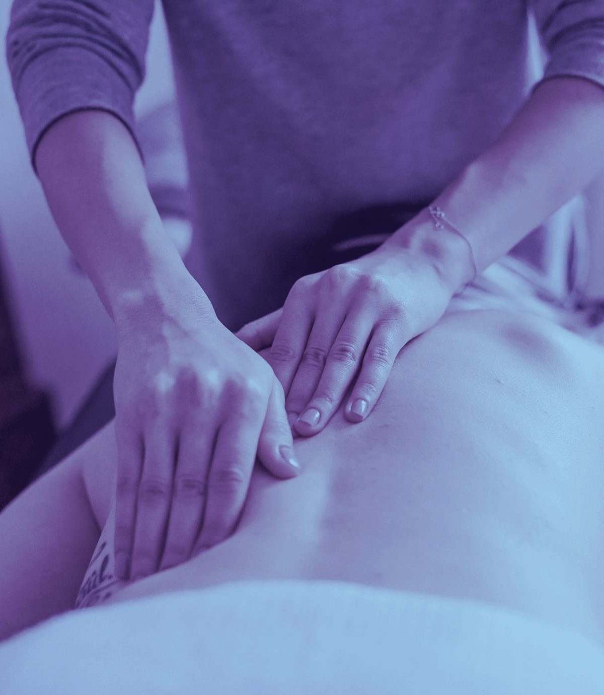 A massage therapist's steady, gentle hands working along a client's back, bathed in a soft violet-blue light