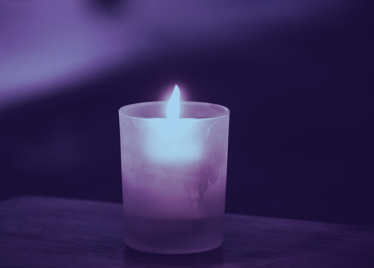 A single candle glowing softly in a dim, calm room with a cool violet cast