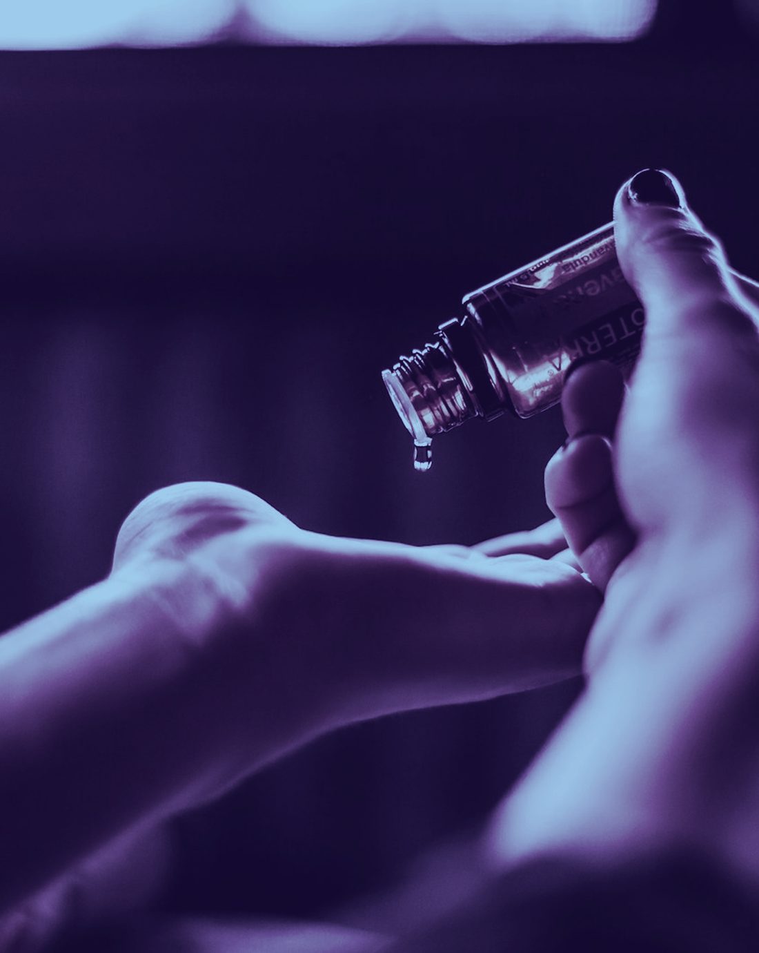 Hands cradling a small bottle of massage oil in moody, cool-toned light