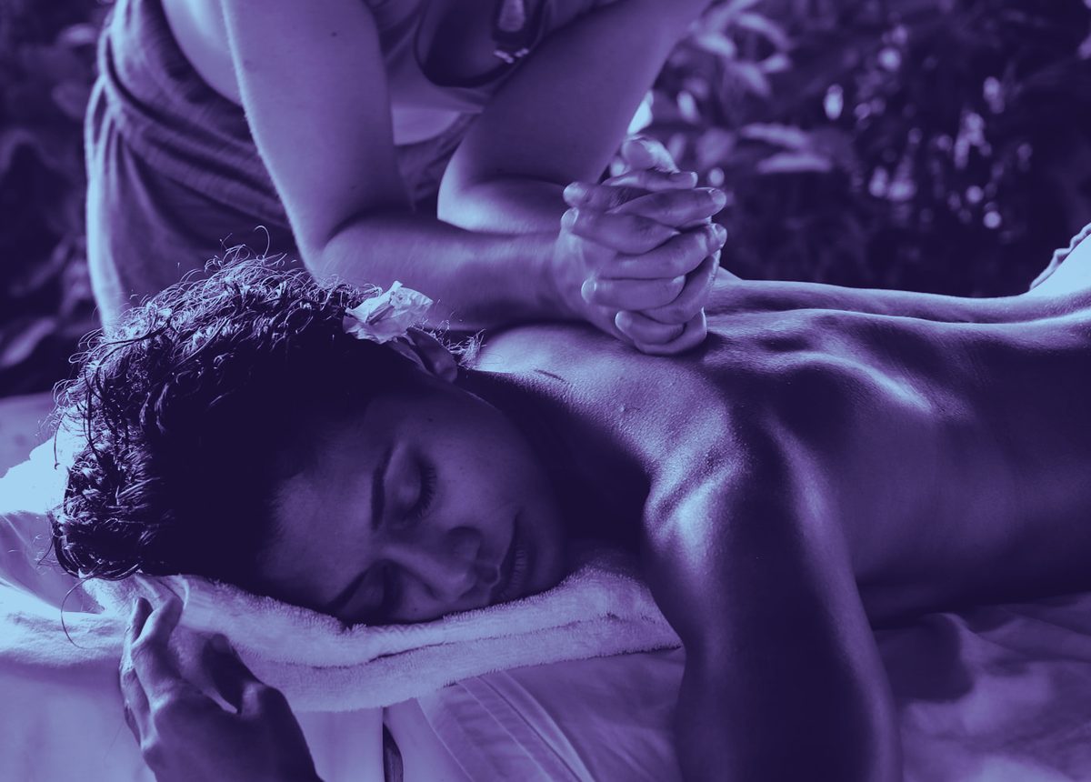 Steady hands working gently along a client's upper back and shoulder, in soft violet-blue light